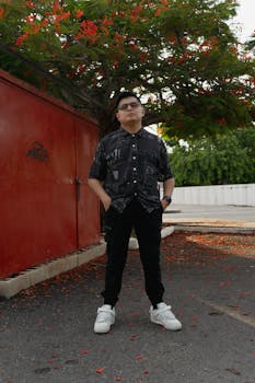 Stylish man posing in a vibrant Merida, Yucatan park under a blooming tree.